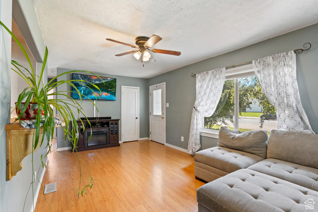 Living area featuring ceiling fan, baseboards, wood finished floors, and a textured ceiling