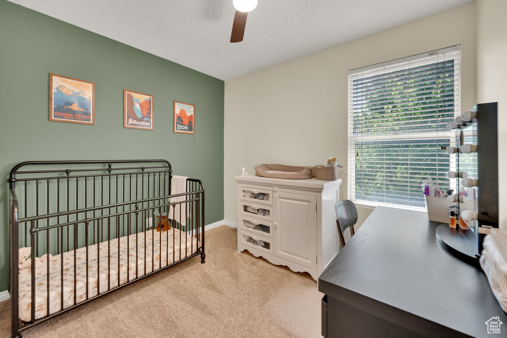 Bedroom with light carpet, a crib, a ceiling fan, and baseboards
