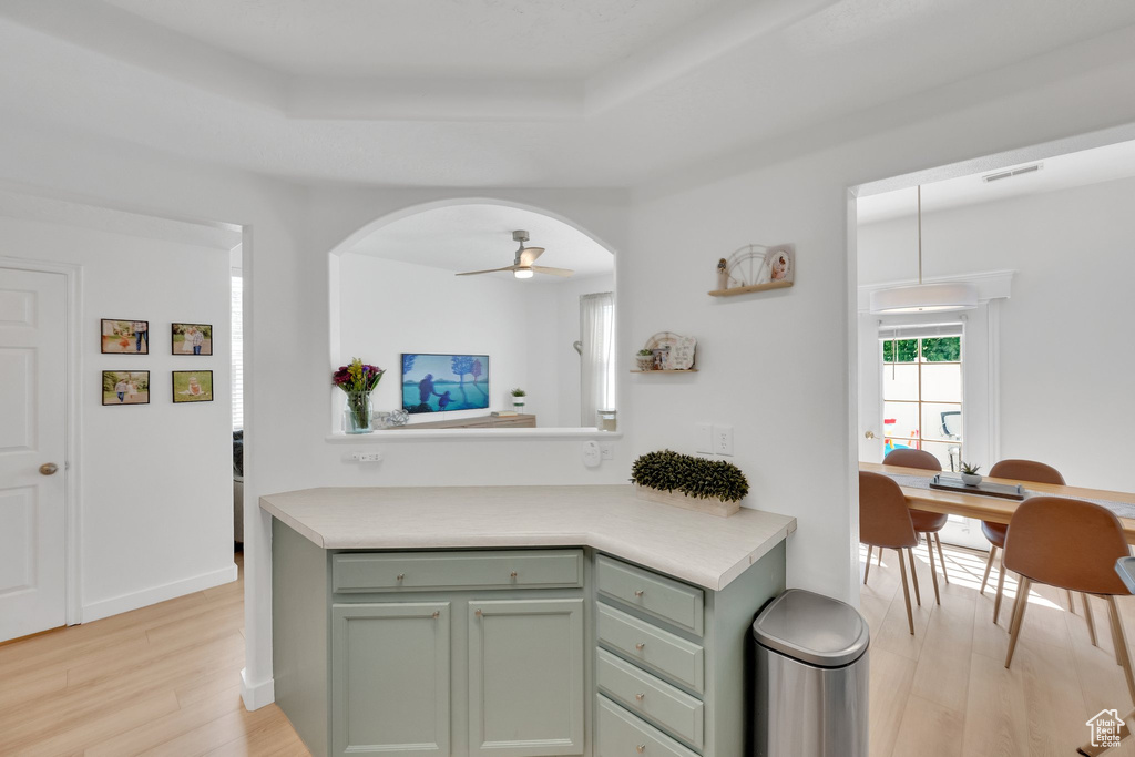 Kitchen featuring green cabinets, light wood-style flooring, arched walkways, and a raised ceiling