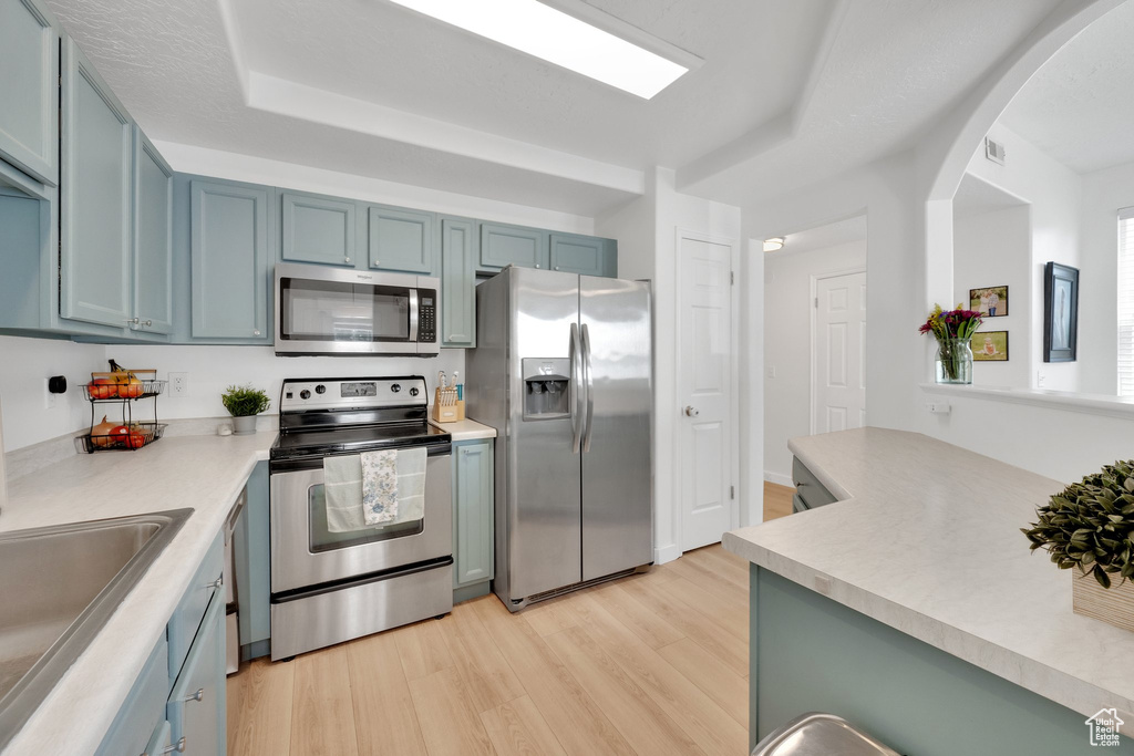 Kitchen featuring appliances with stainless steel finishes, light wood-style flooring, a sink, blue cabinetry, and arched walkways