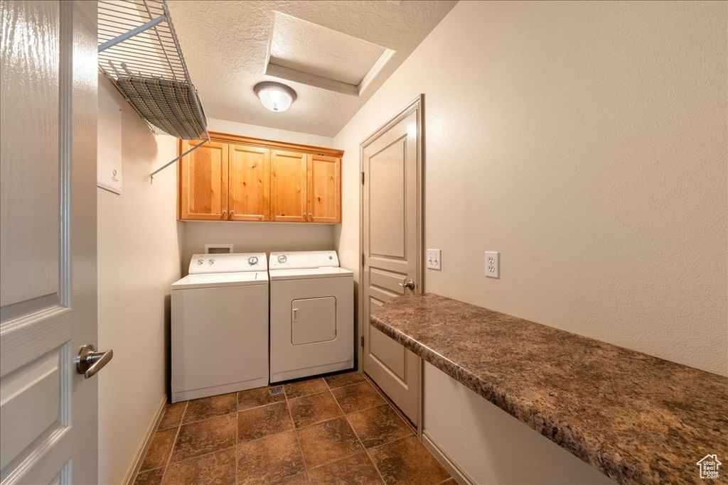 Washroom with cabinet space, washer and dryer, a textured ceiling, dark stone finish flooring, and baseboards