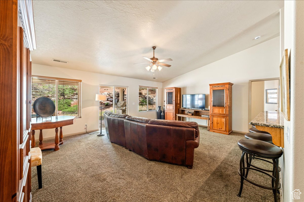 Carpeted living room featuring vaulted ceiling, a ceiling fan, and baseboards