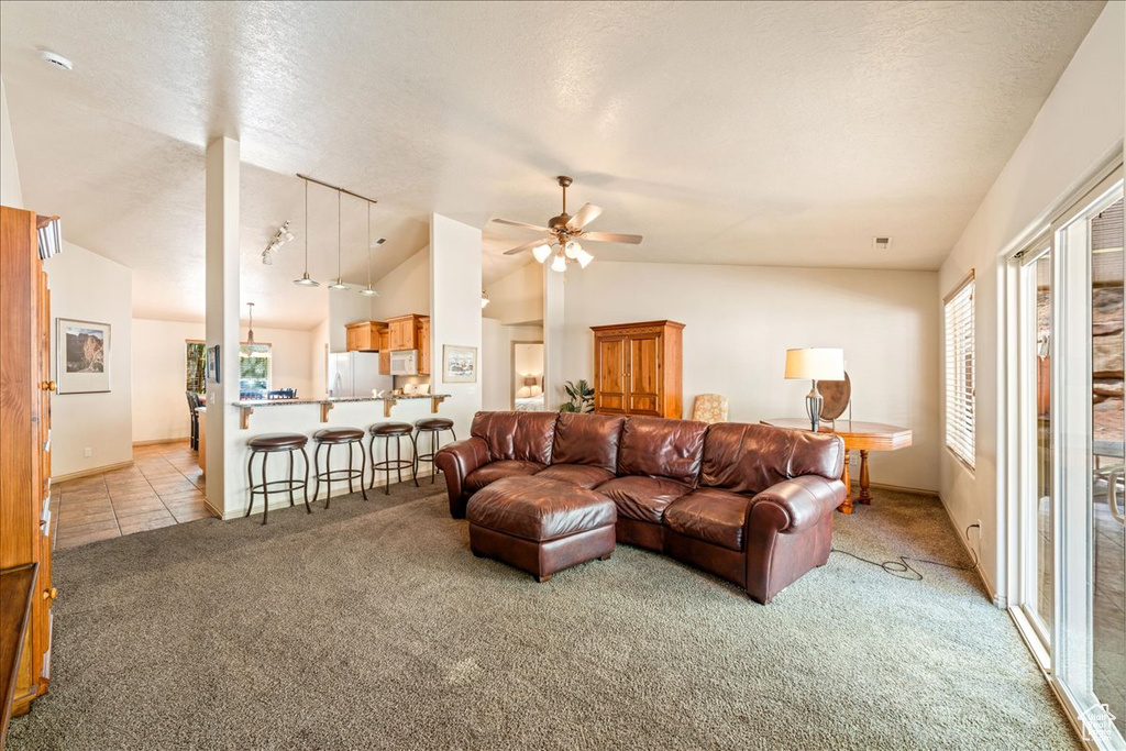 Living room featuring light colored carpet, vaulted ceiling, a ceiling fan, baseboards, and a textured ceiling