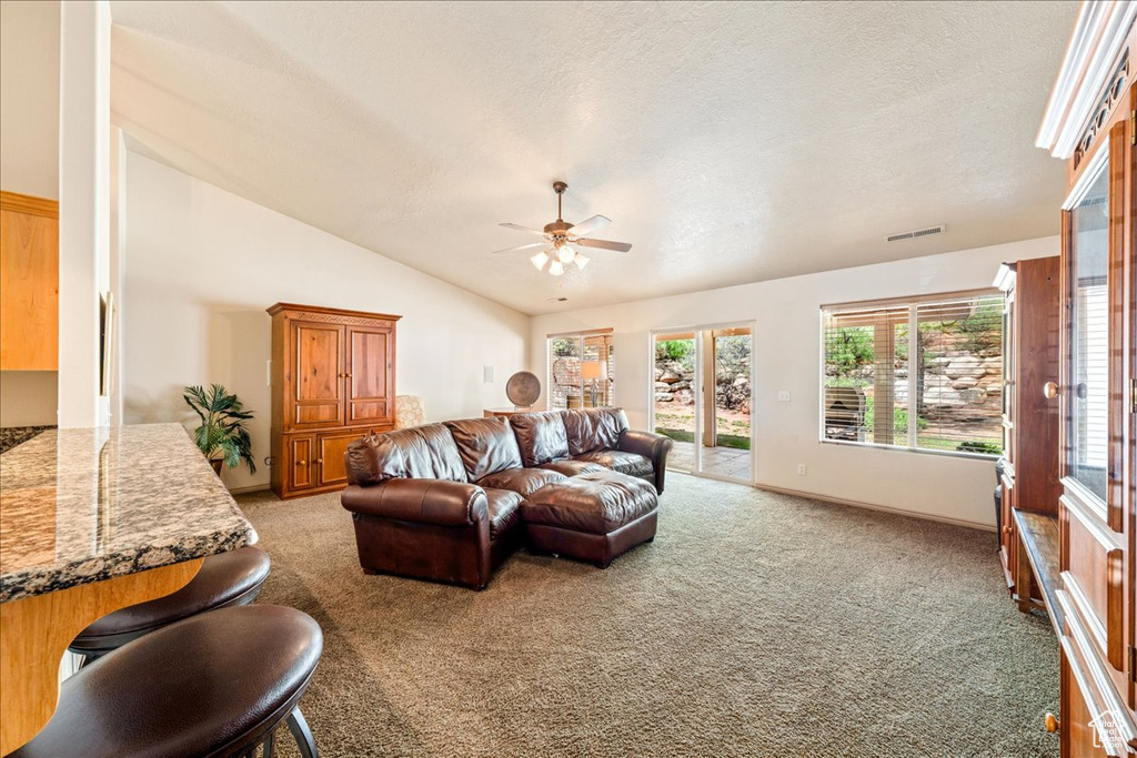 Living area featuring light carpet, a ceiling fan, vaulted ceiling, a textured ceiling, and baseboards