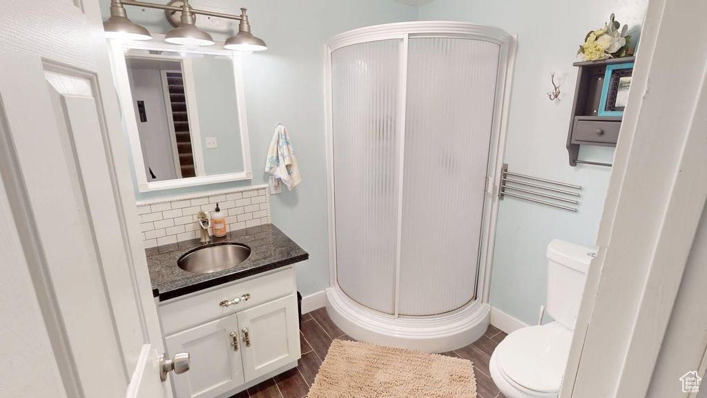 Bathroom with a stall shower, toilet, vanity, wood finished floors, and decorative backsplash
