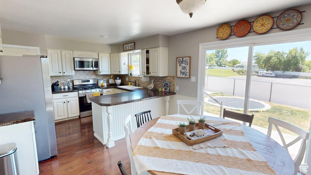 Kitchen featuring appliances with stainless steel finishes, dark countertops, a peninsula, tasteful backsplash, and white cabinets