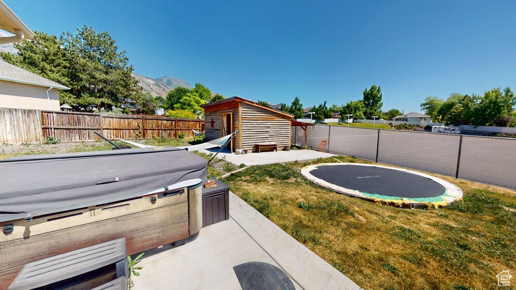 View of yard featuring a hot tub, a trampoline, an outbuilding, a mountain view, and a patio