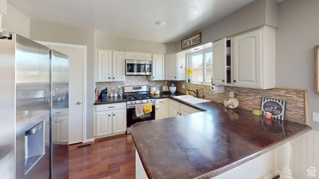 Kitchen with appliances with stainless steel finishes, a sink, dark countertops, a peninsula, and dark wood finished floors