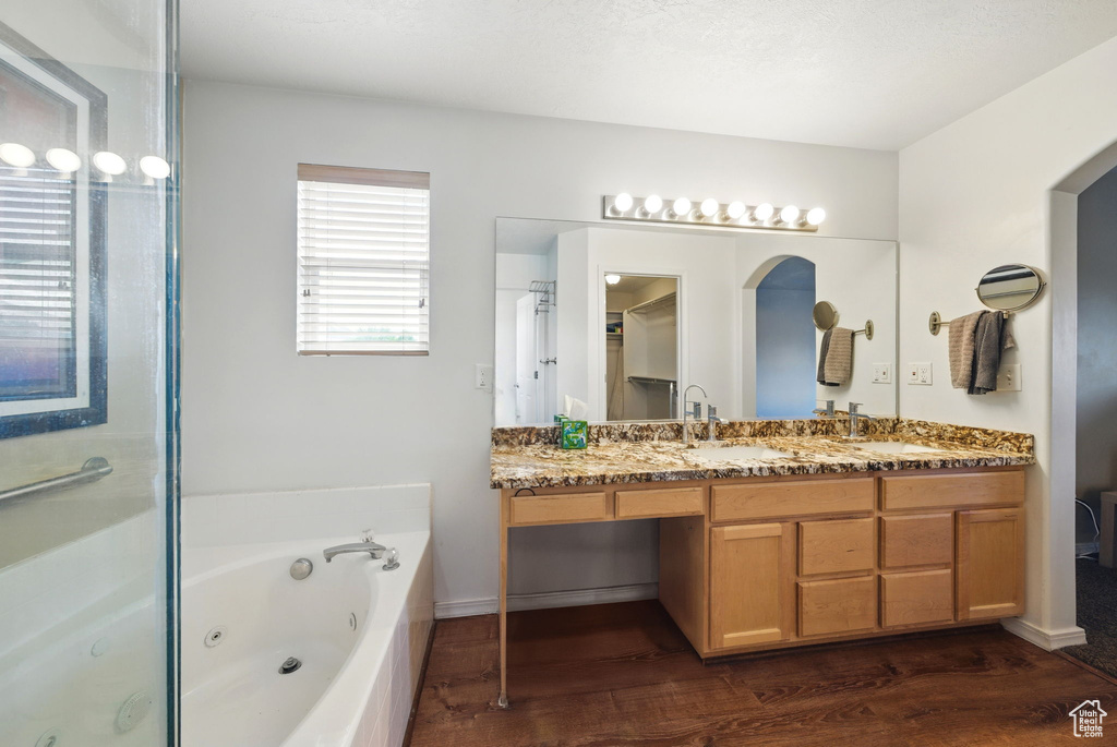 Bathroom with double vanity, a tub with jets, wood finished floors, and baseboards