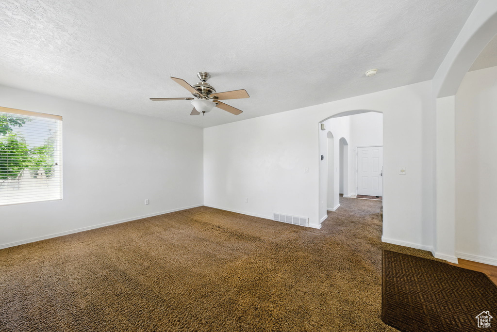Unfurnished room with arched walkways, ceiling fan, carpet flooring, baseboards, and a smoke detector