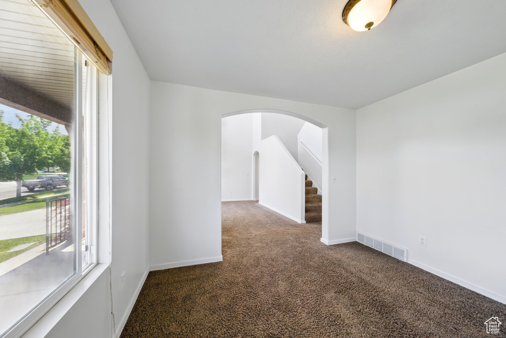 Empty room featuring carpet, arched walkways, and baseboards