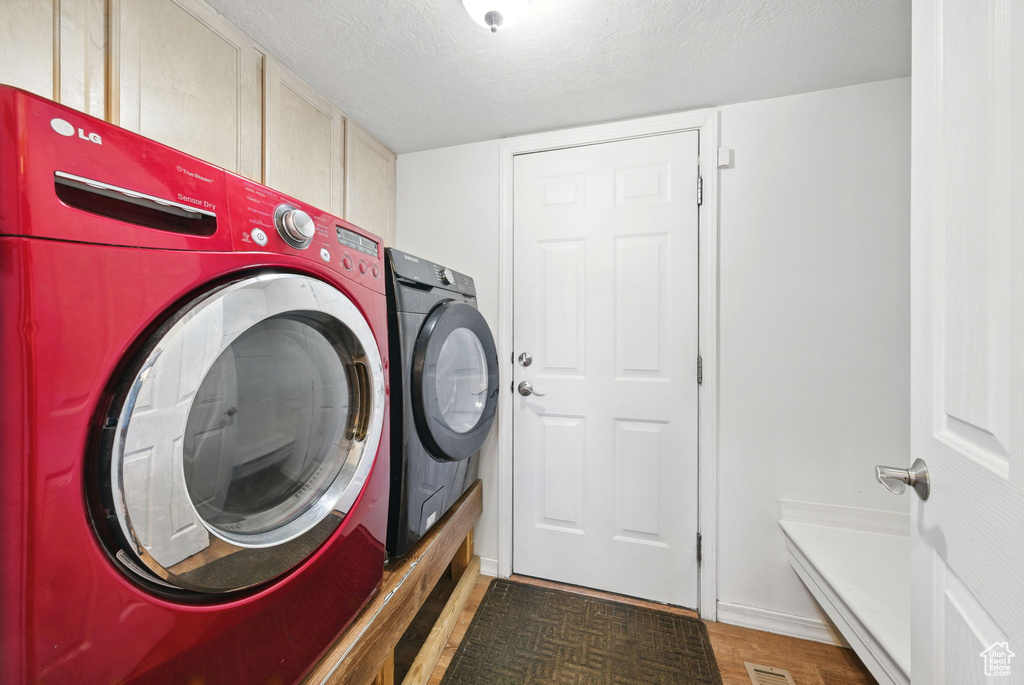 Laundry area featuring separate washer and dryer, cabinet space, a textured ceiling, baseboards, and light wood-style flooring