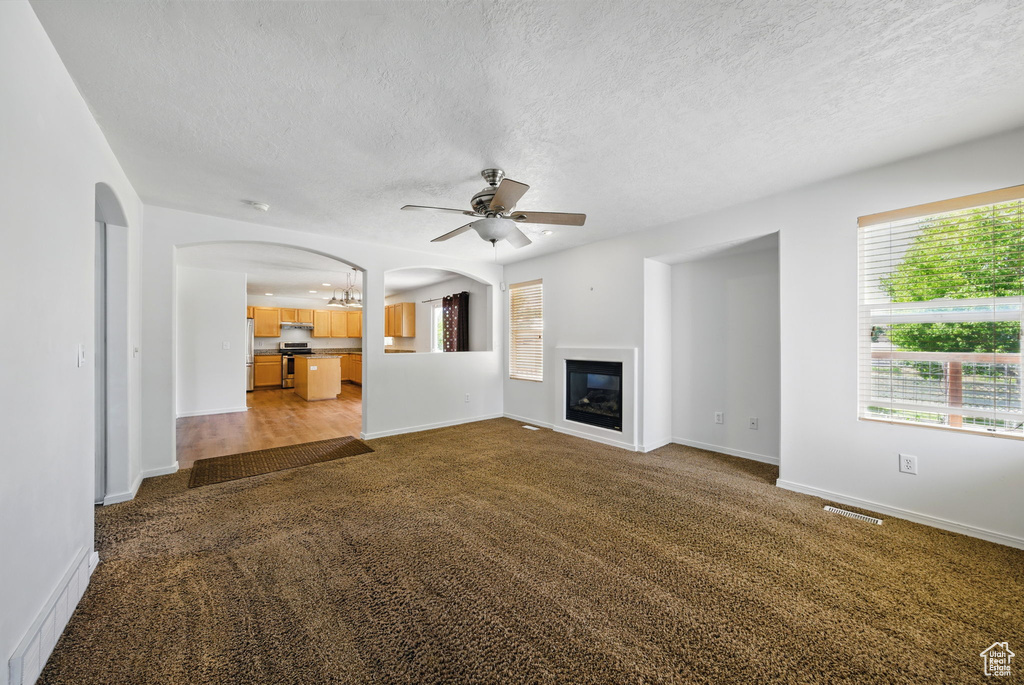 Unfurnished living room featuring arched walkways, carpet, a ceiling fan, a textured ceiling, and a glass covered fireplace