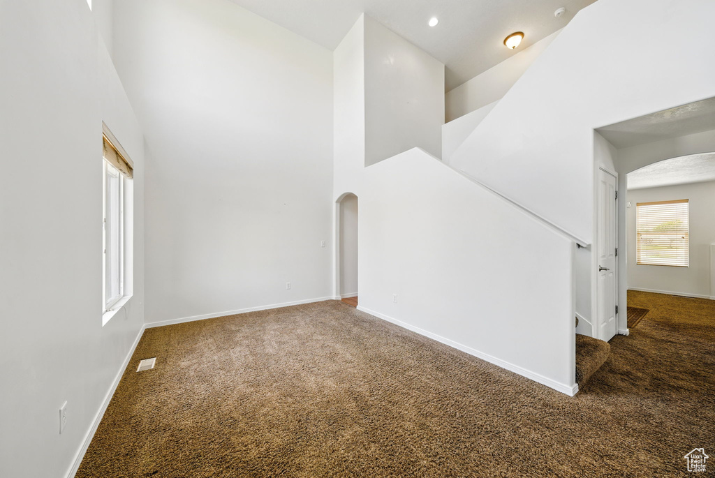 Spare room featuring arched walkways, carpet floors, a high ceiling, and baseboards