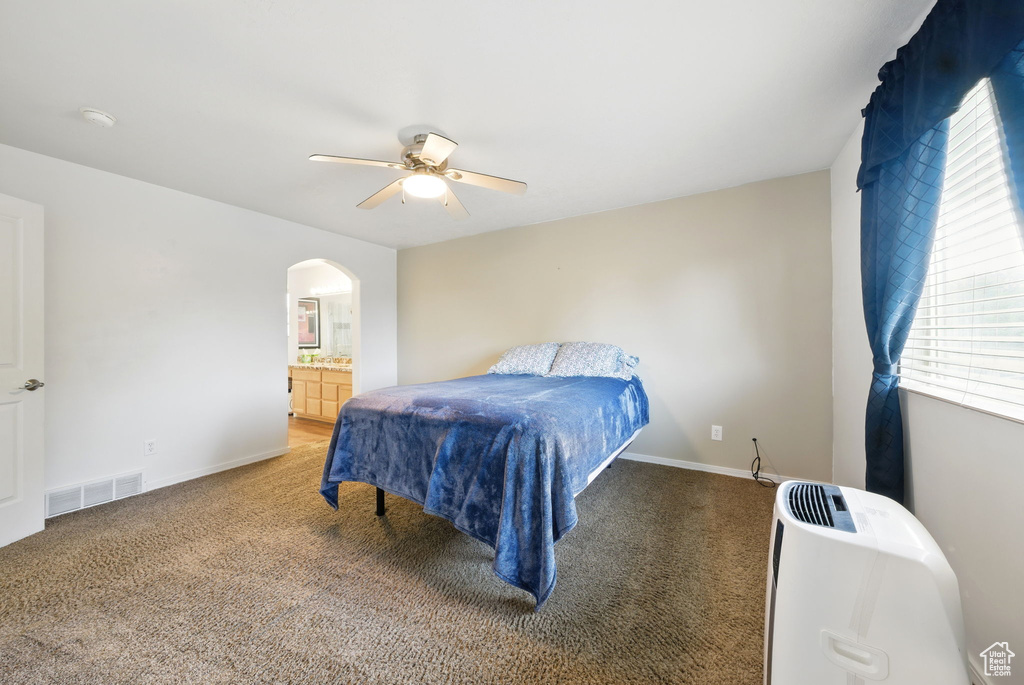 Bedroom with arched walkways, light colored carpet, baseboards, a ceiling fan, and ensuite bathroom