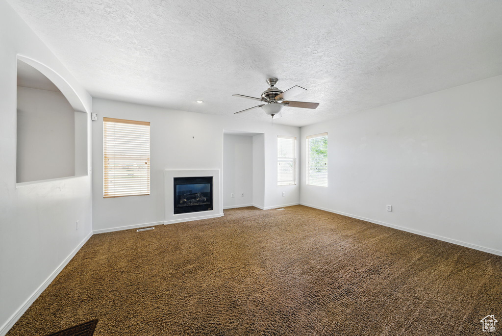 Unfurnished living room with carpet floors, a glass covered fireplace, ceiling fan, a textured ceiling, and baseboards