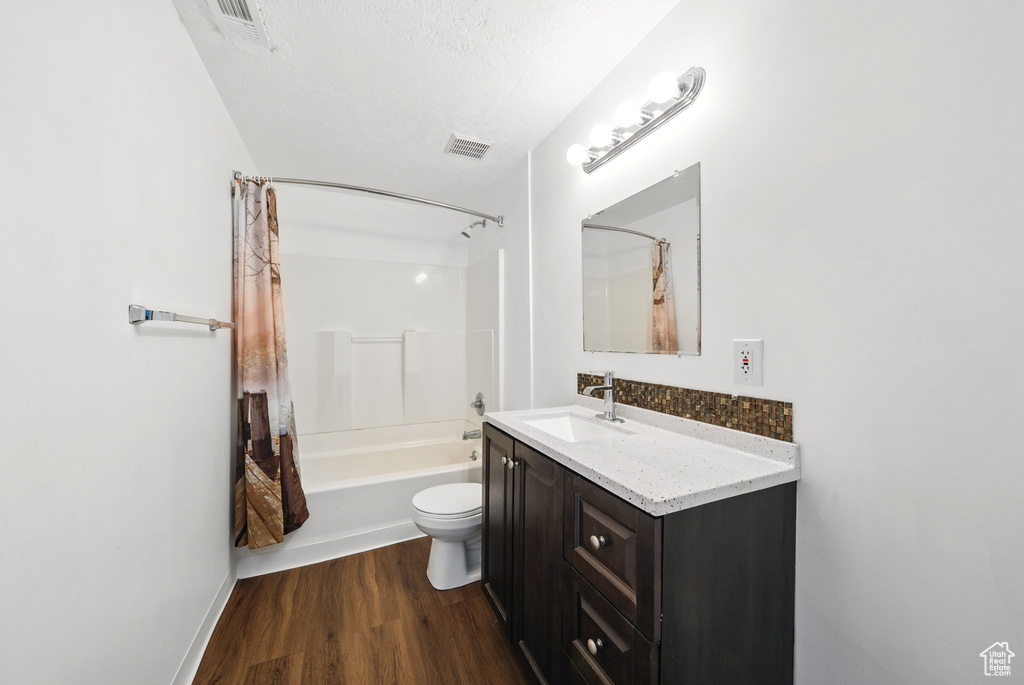 Full bathroom with vanity, wood finished floors, shower / bath combination with curtain, and toilet
