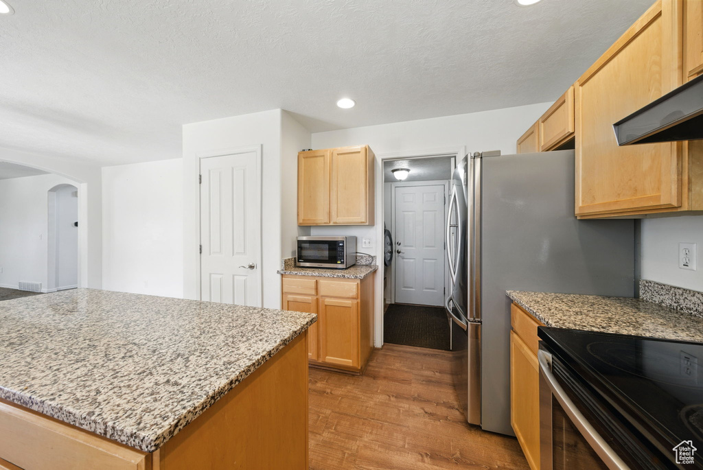 Kitchen with appliances with stainless steel finishes, arched walkways, recessed lighting, light wood-style floors, and light brown cabinetry