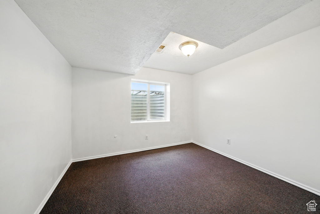 Empty room with baseboards, dark carpet, and a textured ceiling