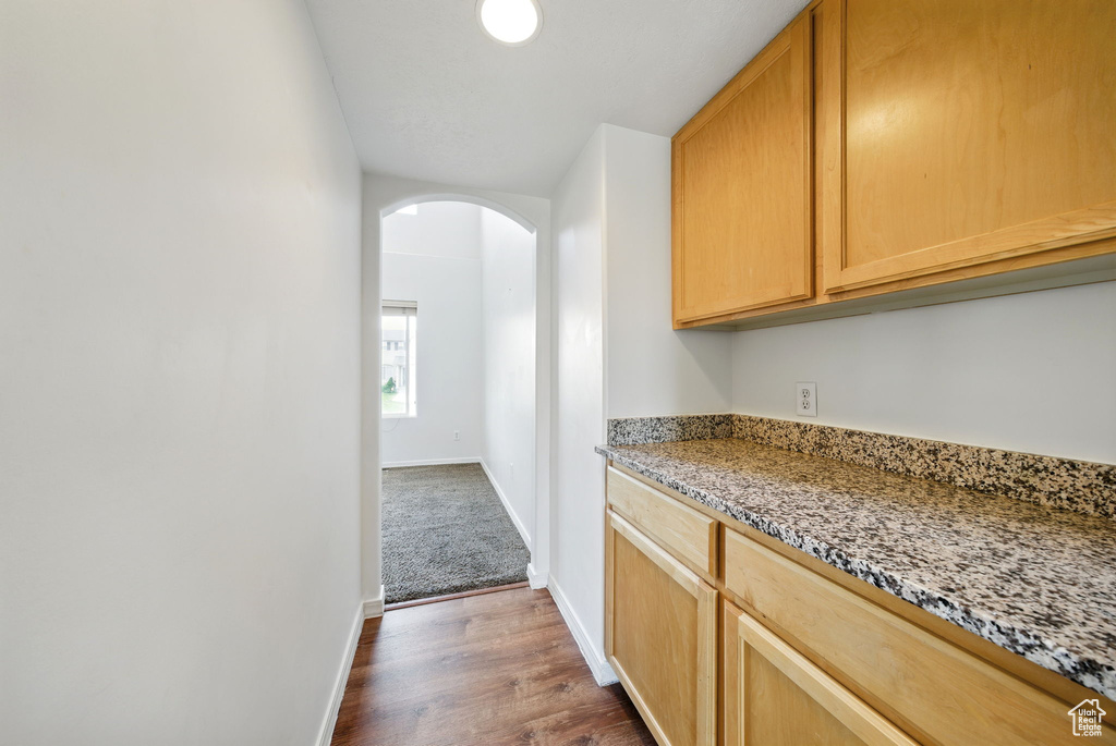 Kitchen featuring arched walkways, light stone countertops, dark wood finished floors, and baseboards