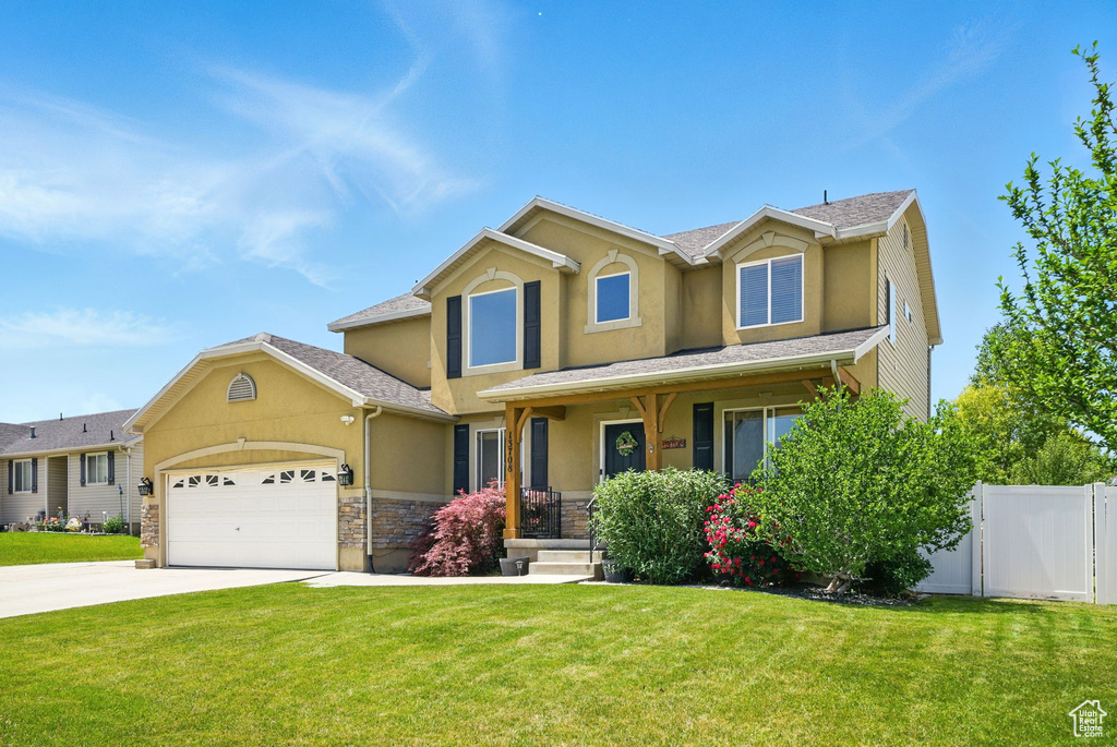 Traditional home featuring stucco siding, an attached garage, covered porch, concrete driveway, and stone siding