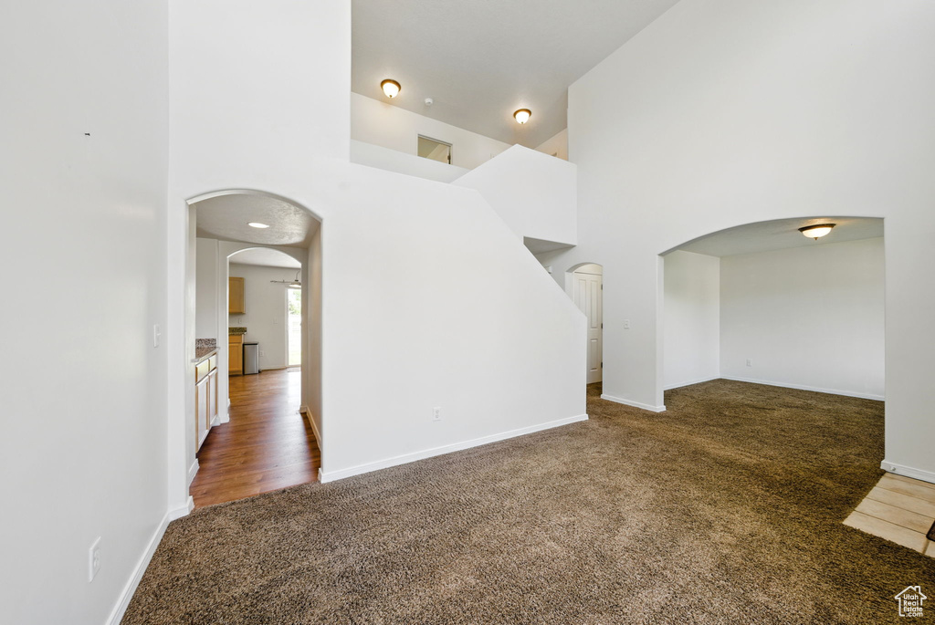 Unfurnished living room featuring carpet floors, arched walkways, a high ceiling, and baseboards