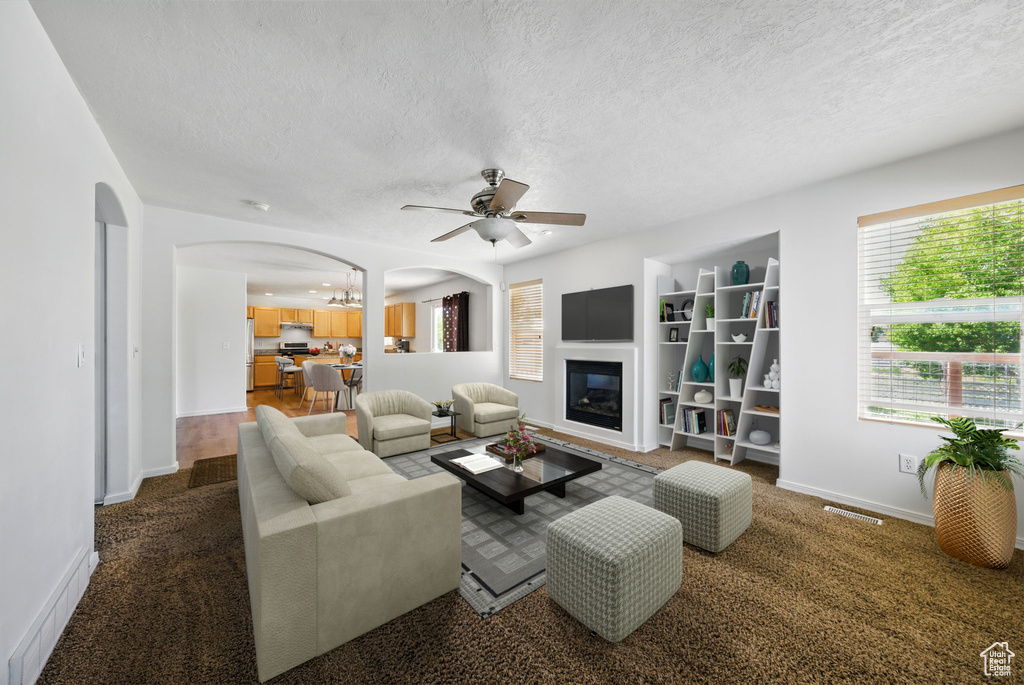 Living room with arched walkways, a textured ceiling, ceiling fan, baseboards, and a glass covered fireplace