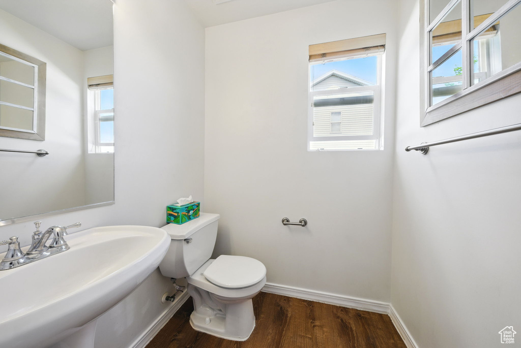 Half bath with toilet, wood finished floors, healthy amount of natural light, and baseboards
