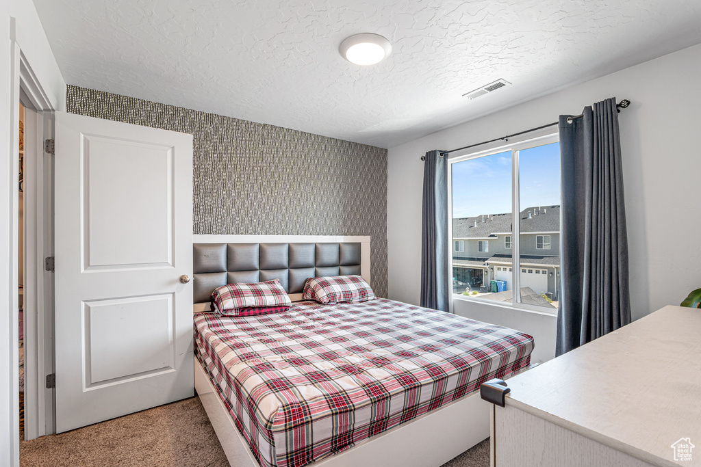 Bedroom with carpet floors, a textured ceiling, and wallpapered walls