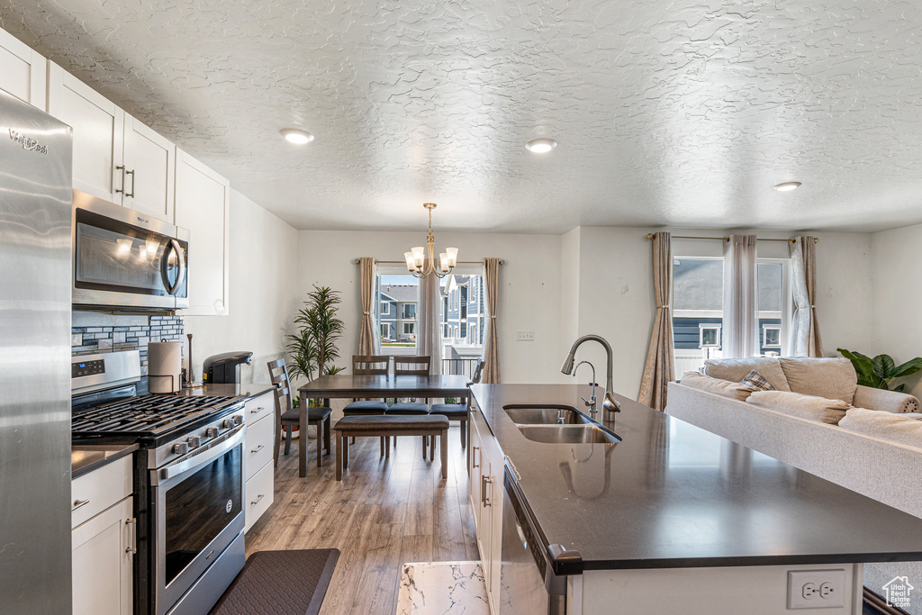 Kitchen featuring appliances with stainless steel finishes, dark countertops, a sink, a kitchen island with sink, and plenty of natural light