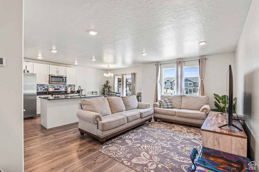 Living room featuring wood finished floors, a chandelier, a textured ceiling, and recessed lighting
