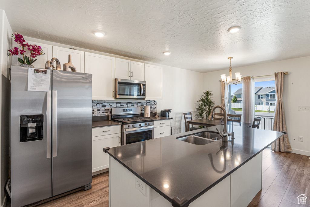 Kitchen featuring appliances with stainless steel finishes, a sink, dark countertops, a chandelier, and white cabinets