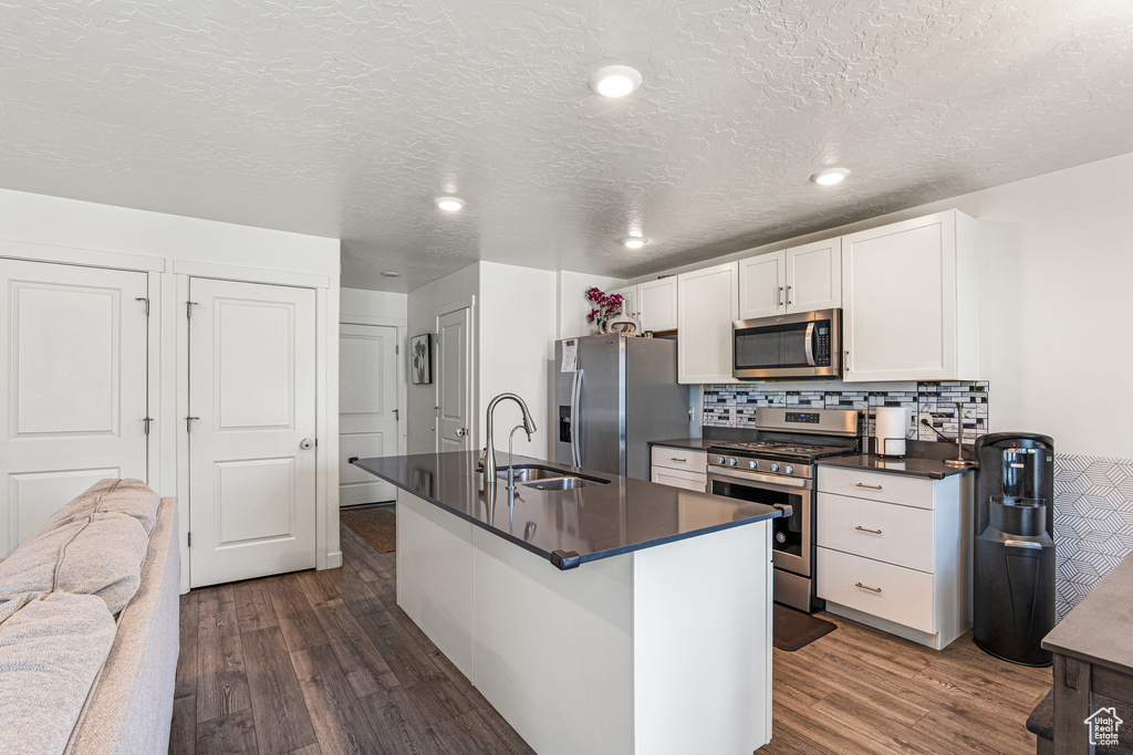 Kitchen featuring stainless steel appliances, dark countertops, dark wood-style flooring, a sink, and a textured ceiling