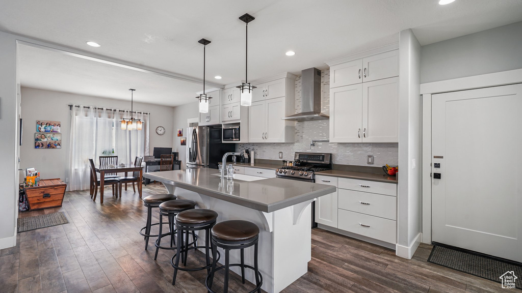 Kitchen featuring wall chimney exhaust hood, appliances with stainless steel finishes, a sink, dark wood-style floors, and tasteful backsplash