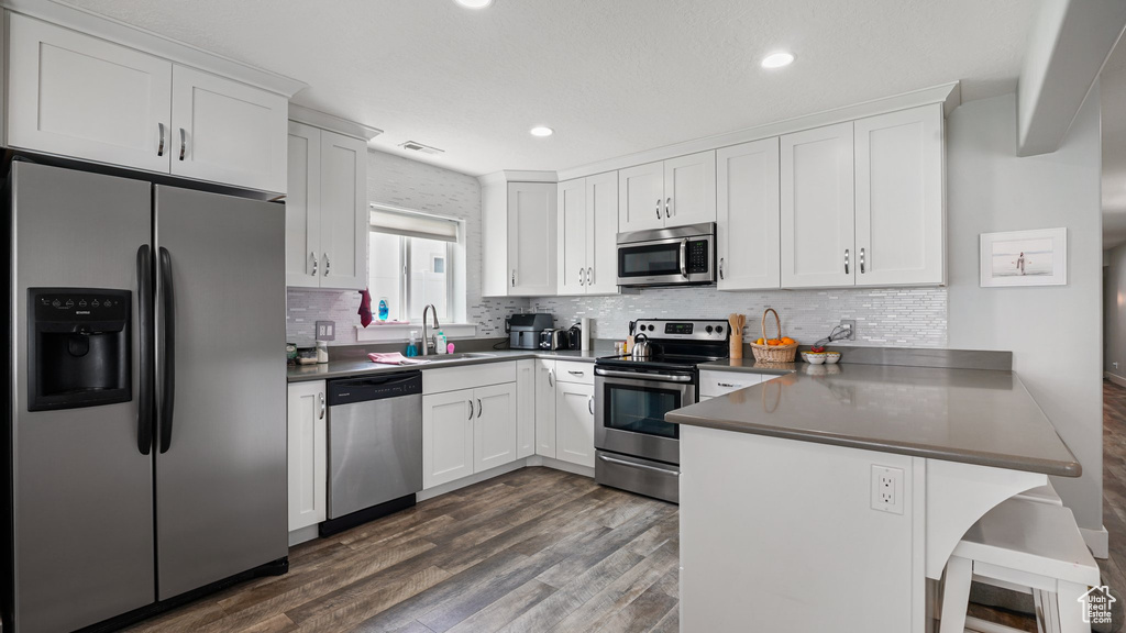 Kitchen featuring appliances with stainless steel finishes, a peninsula, dark countertops, white cabinets, and recessed lighting