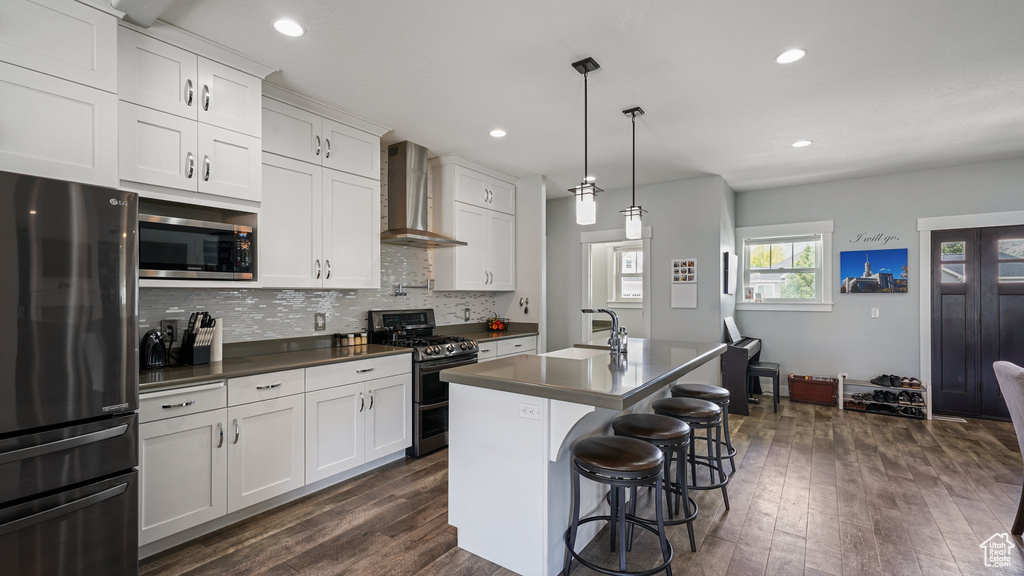 Kitchen with stainless steel appliances, wall chimney exhaust hood, dark countertops, dark wood finished floors, and tasteful backsplash