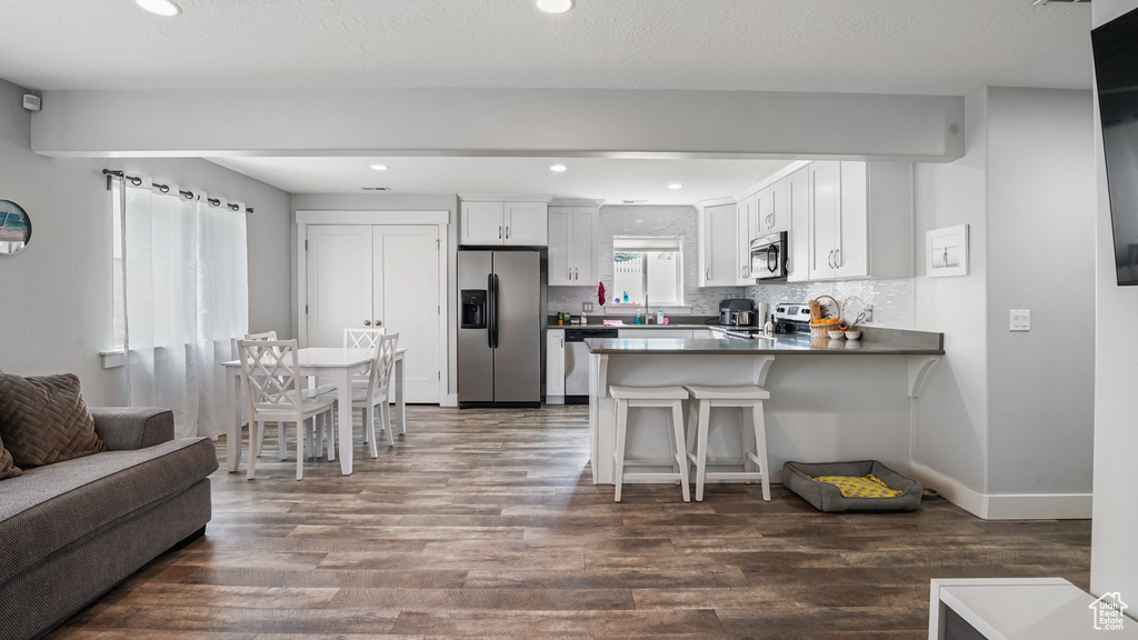 Kitchen featuring stainless steel appliances, a peninsula, dark wood-type flooring, open floor plan, and white cabinetry