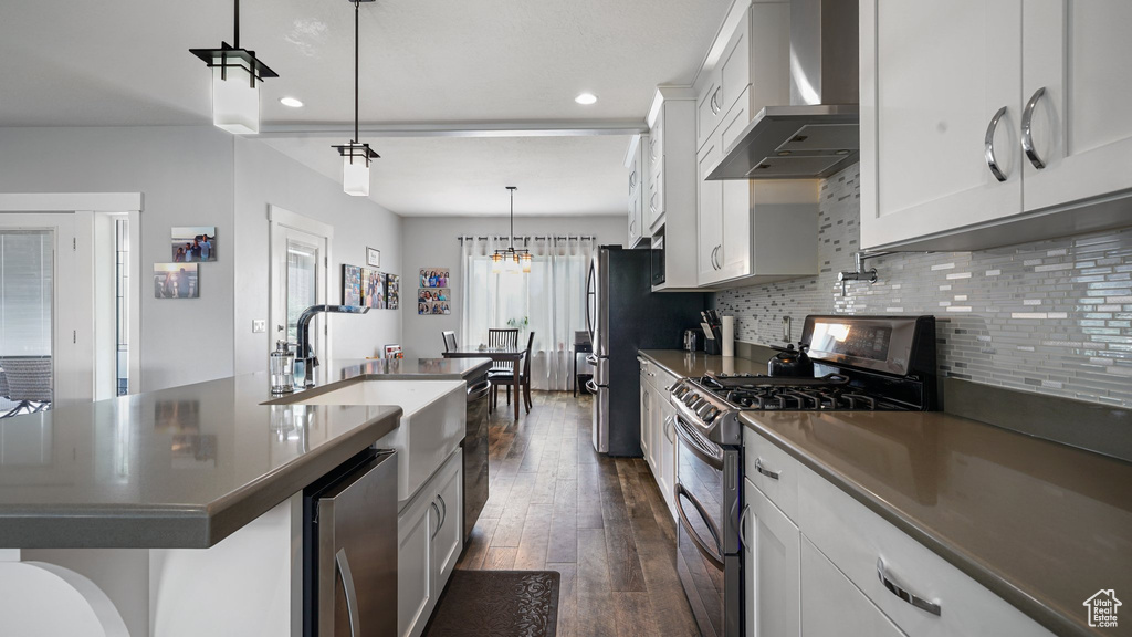Kitchen with appliances with stainless steel finishes, wall chimney exhaust hood, a sink, dark wood-style floors, and backsplash