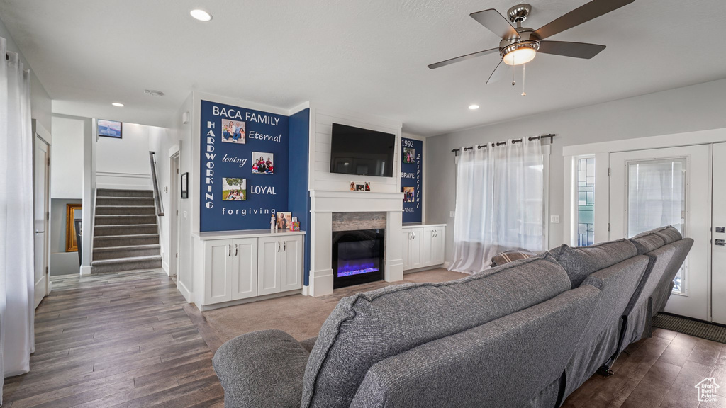 Living room featuring a ceiling fan, stairs, wood finished floors, a fireplace, and recessed lighting