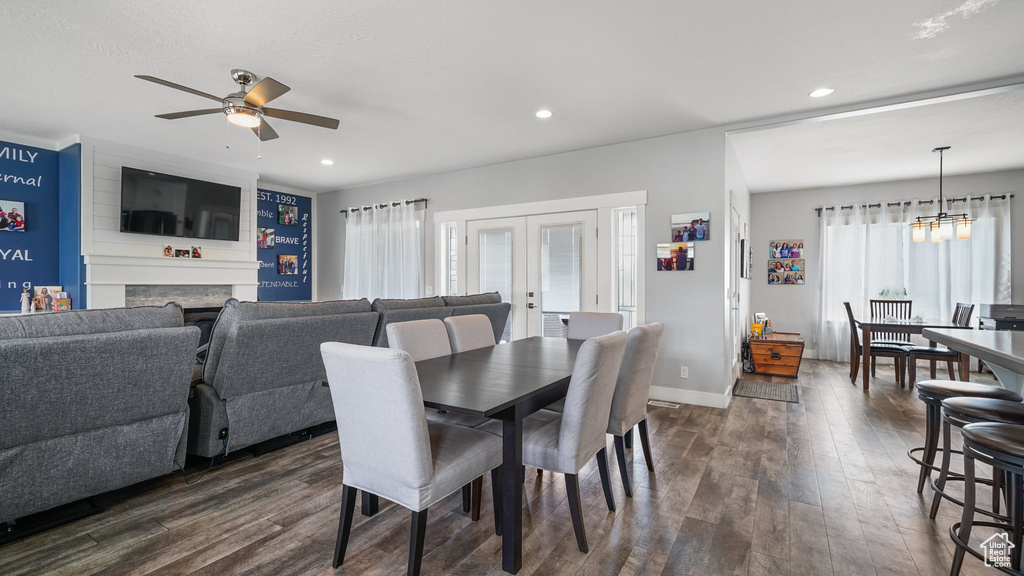 Dining space with dark wood finished floors, ceiling fan, a large fireplace, recessed lighting, and a chandelier