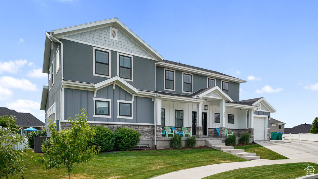 View of front facade featuring board and batten siding, driveway, stone siding, a front yard, and an attached garage