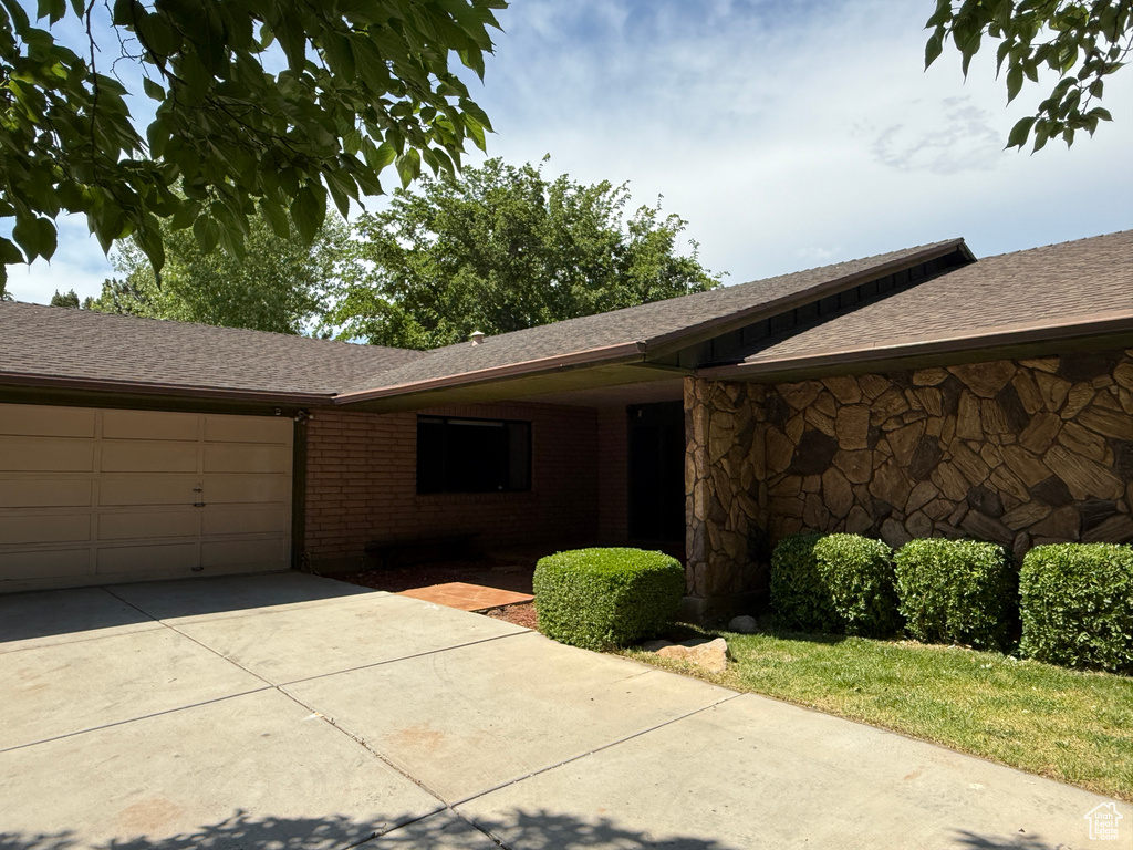 View of front facade with concrete driveway, an attached garage, a shingled roof, and brick siding