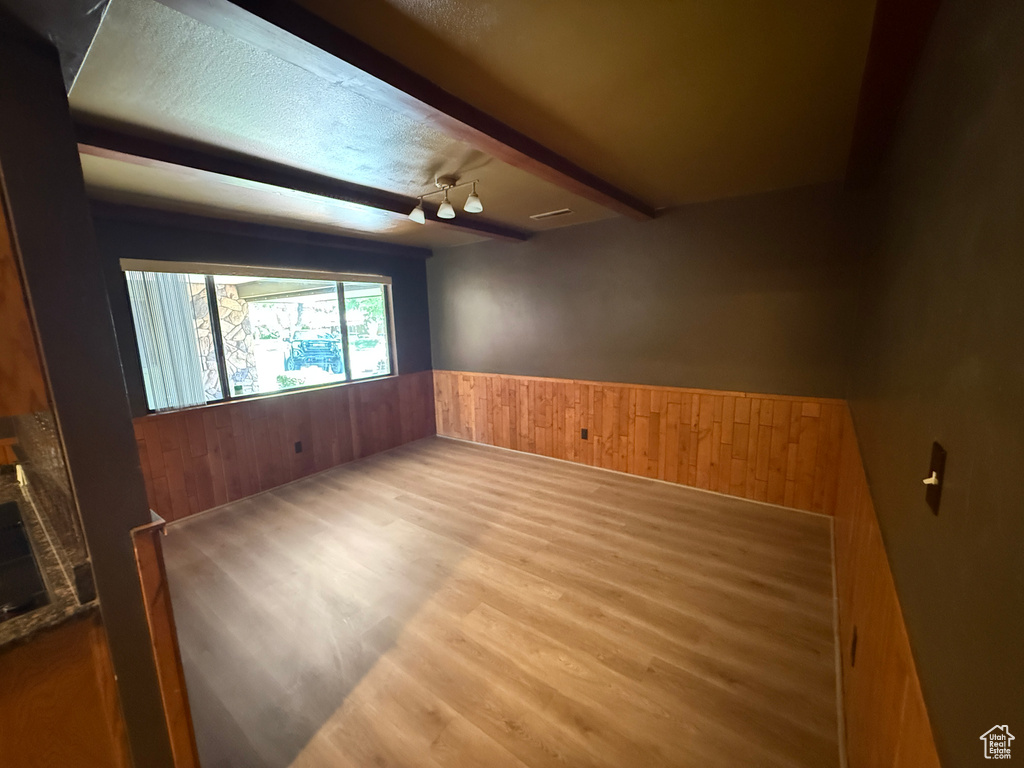 Unfurnished room featuring wood walls, wainscoting, wood finished floors, beamed ceiling, and a fireplace