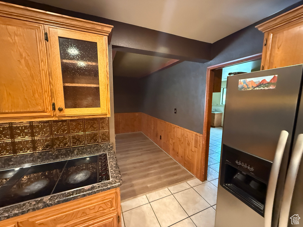 Kitchen featuring stainless steel fridge, wainscoting, light tile patterned flooring, glass insert cabinets, and brown cabinetry