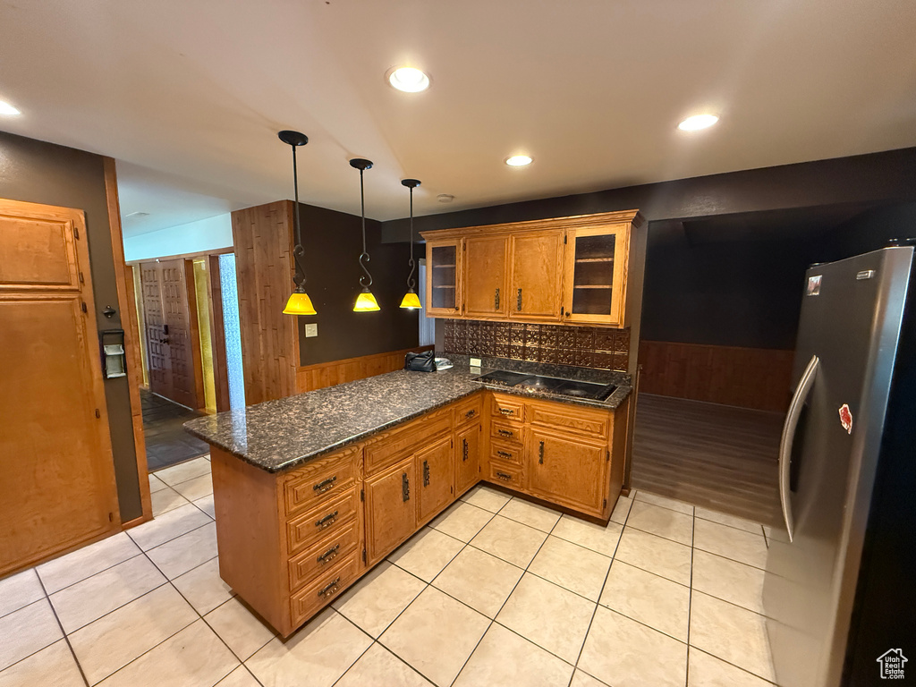 Kitchen featuring freestanding refrigerator, a peninsula, brown cabinetry, tasteful backsplash, and glass insert cabinets