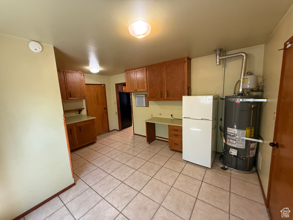 Kitchen featuring freestanding refrigerator, gas water heater, light tile patterned flooring, brown cabinets, and light countertops