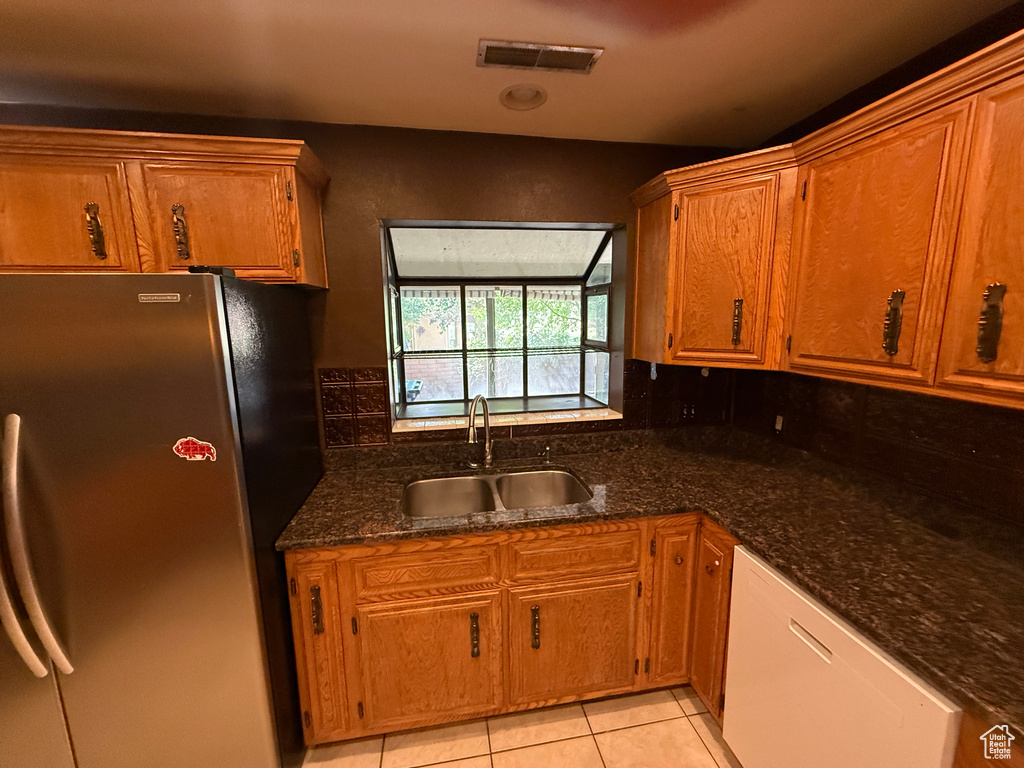 Kitchen featuring freestanding refrigerator, a sink, dishwasher, light tile patterned flooring, and brown cabinetry