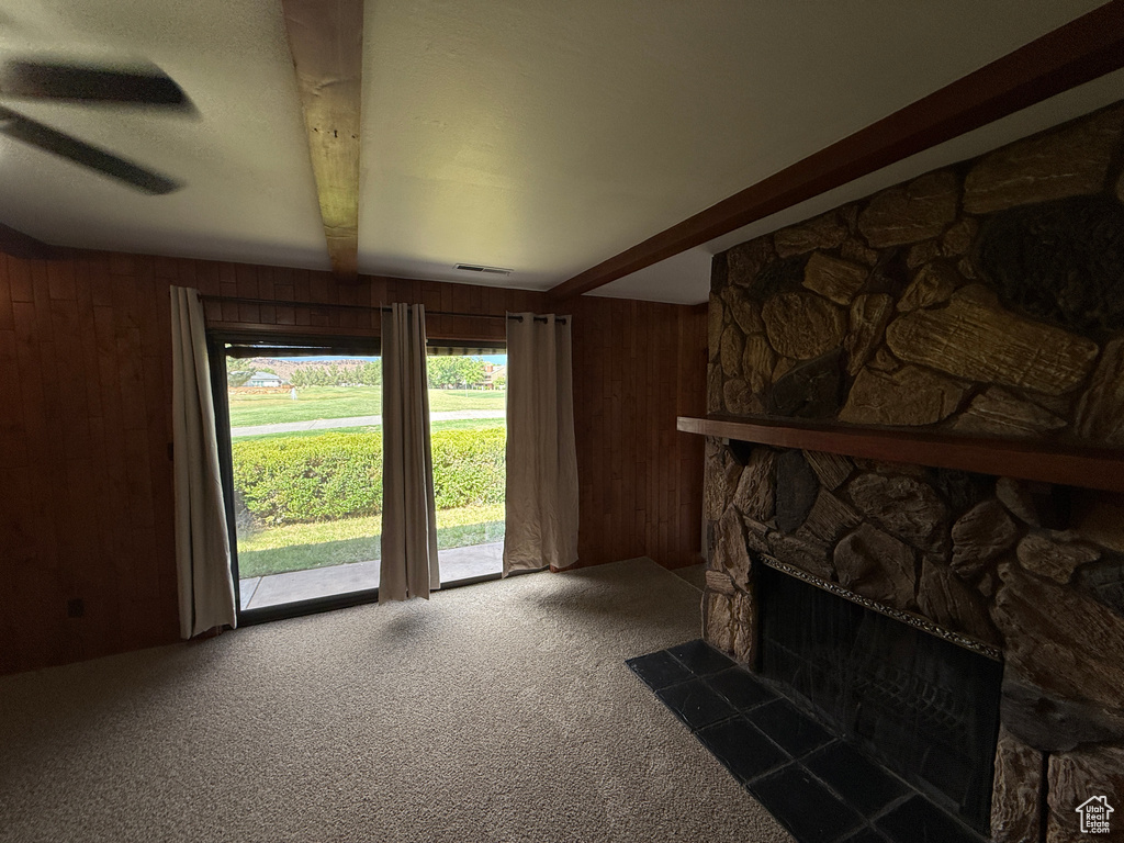 Unfurnished living room featuring beamed ceiling, wood walls, carpet, and a fireplace