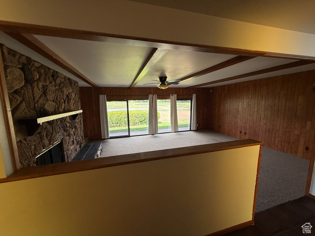 Unfurnished living room featuring wood walls, a ceiling fan, a fireplace, and beam ceiling