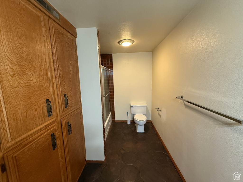 Bathroom with toilet, baseboards, and shower / bath combination with glass door